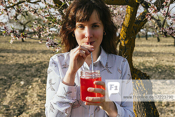 Junge Frau trinkt Erdbeerlimonade am Mandelbaum