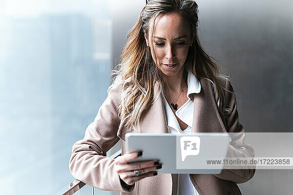 Smiling female professional using digital tablet while leaning on railing