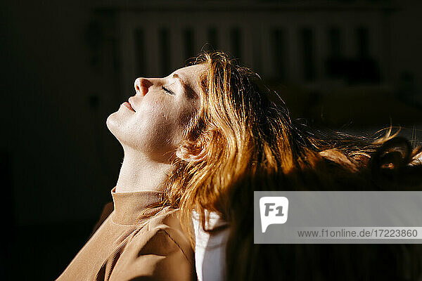 Lächelnde Frau mit geneigtem Kopf zu Hause im Sonnenlicht