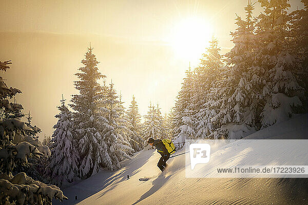 Mittlerer erwachsener Mann beim Skifahren auf einem verschneiten Berg bei Sonnenaufgang