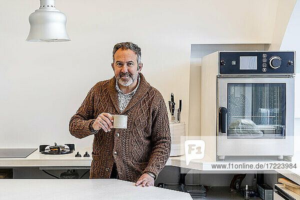 Lächelnder Mann mit Kaffeetasse in der Küche zu Hause stehend