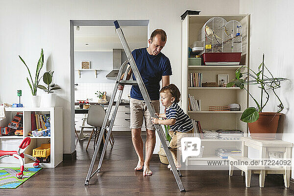 Cute toddler climbing ladder being held by father in playroom at home