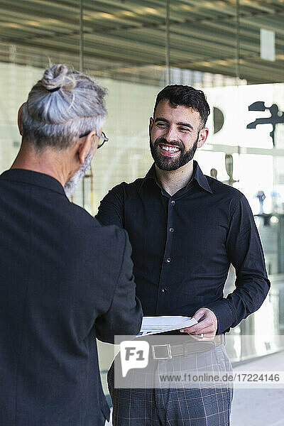Smiling young businessman discussing with male colleague at entrance