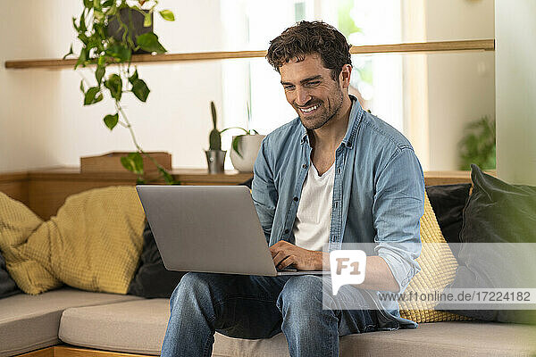 Happy male freelance worker using laptop on couch at home