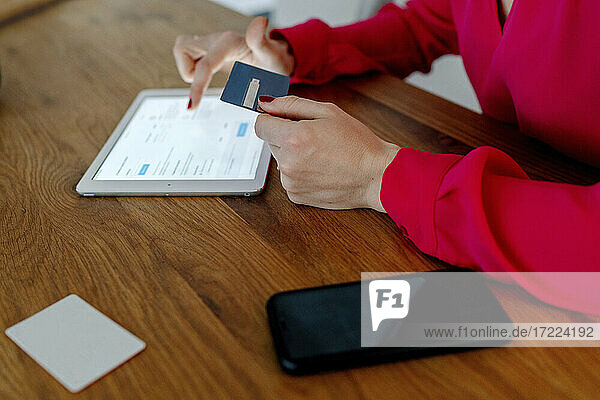 Frau bei der Kartenzahlung beim Einkauf im Internet mit digitalem Tablet am Tisch