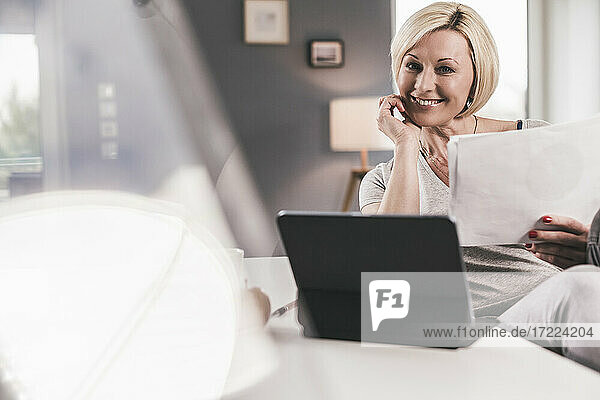Lächelnde Frau mit digitalem Tablet und Papier zu Hause