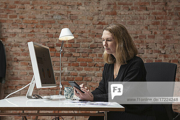 Unternehmerin mit Mobiltelefon am Schreibtisch im Büro