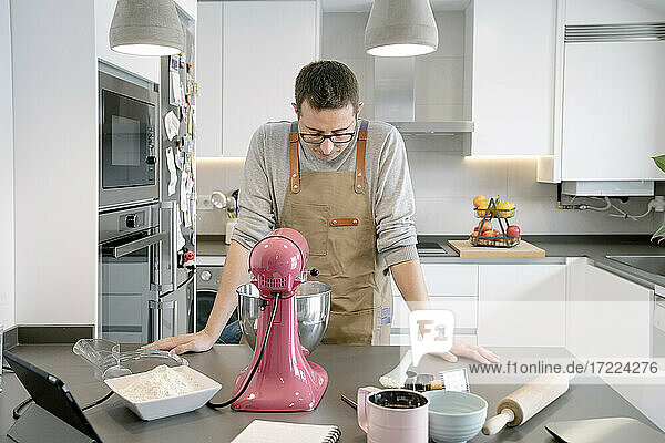 Mid adult man with apron looking at stand mixer while preparing food at home
