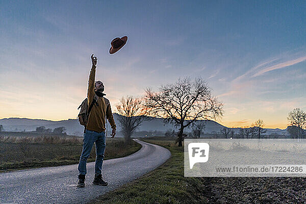 Man throwing hat in mid air while standing on country road