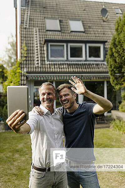 Vater und Sohn führen ein Videogespräch über ein digitales Tablet  während sie im Hinterhof stehen