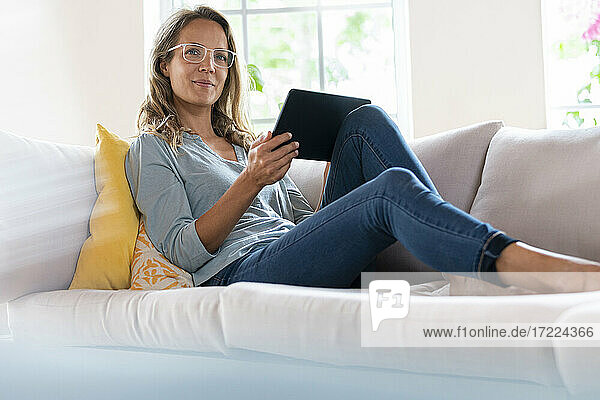 Schöne Frau mit digitalem Tablet entspannt auf Sofa im Wohnzimmer