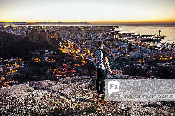 Man looking at city view while standing on stool during sunrise