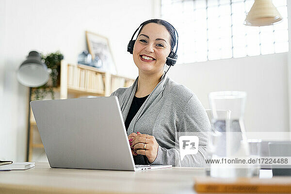 Smiling businesswoman wearing headphones while working at home