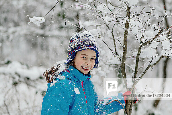 Smiling girl shaking a snowy tree