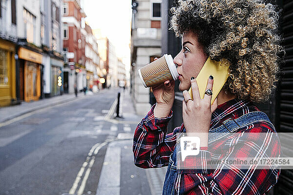 Junge Frau trinkt Kaffee  während sie mit einem Mobiltelefon spricht