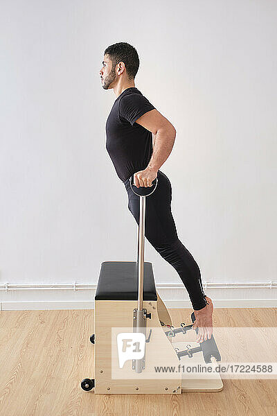 Man practicing pilates on chair by wall in exercise room