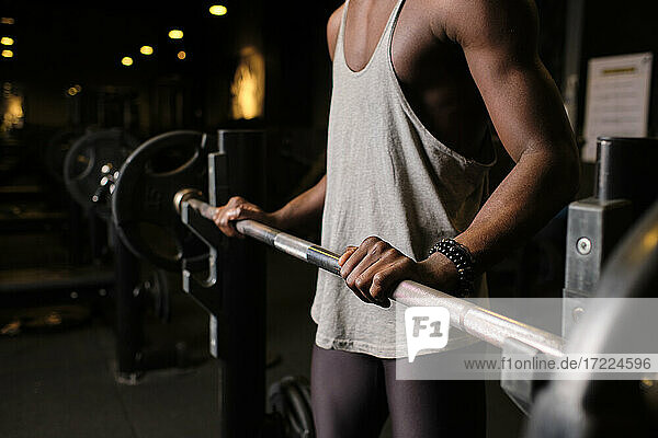 Young man preparing to lift barbell while exercising in gym