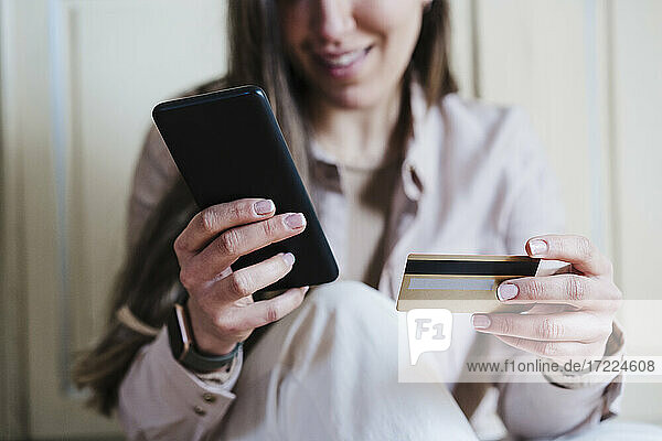 Frau  die ein Smartphone benutzt  während sie eine Kreditkarte zu Hause hält