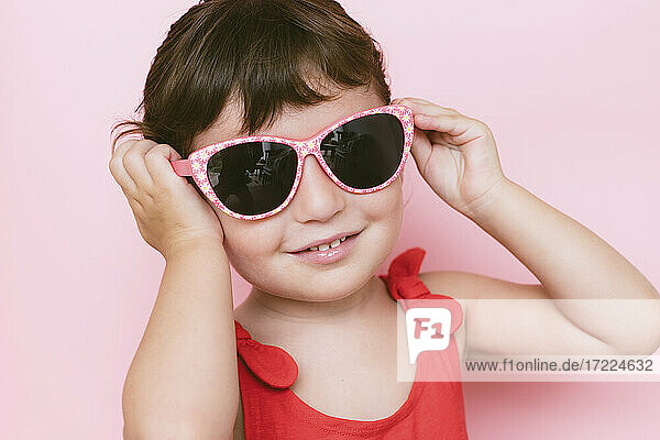 Portrait of smiling little girl wearing sunglasses against pink background
