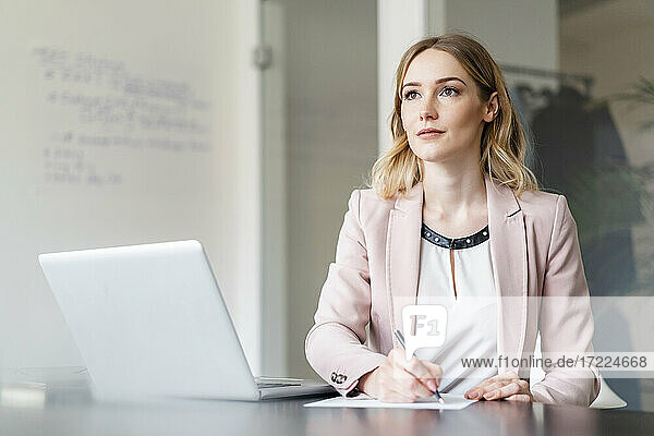 Geschäftsfrau beim Nachdenken über ein Dokument  das sie mit einem Laptop im Büro schreibt
