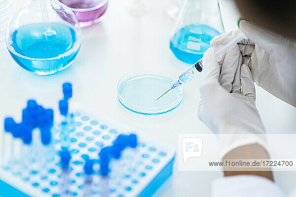 Forscher  der im Labor mit einer Spritze Flüssigkeit aus einer Petrischale aufzieht