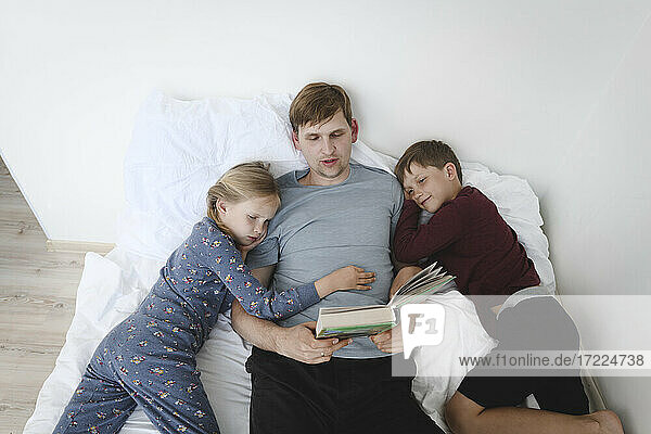 Father reading book with daughter and son in bed