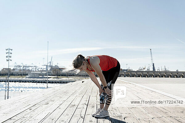 Young female athlete resting on pier during sunny day