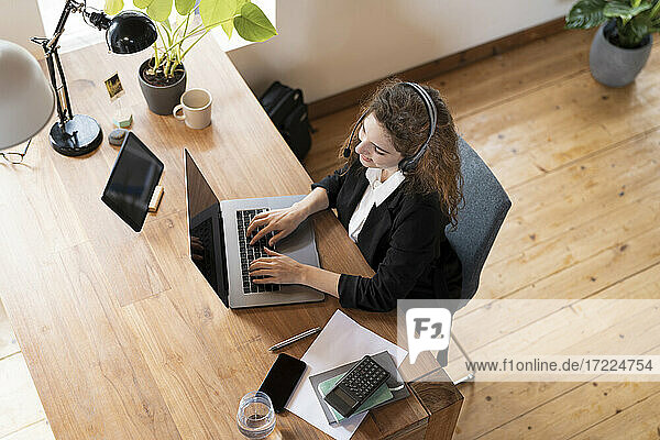 Female customer service representative with headphones speaking to client while working at laptop in home office