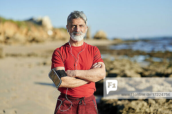 Confident man with arms crossed standing at beach during sunny day