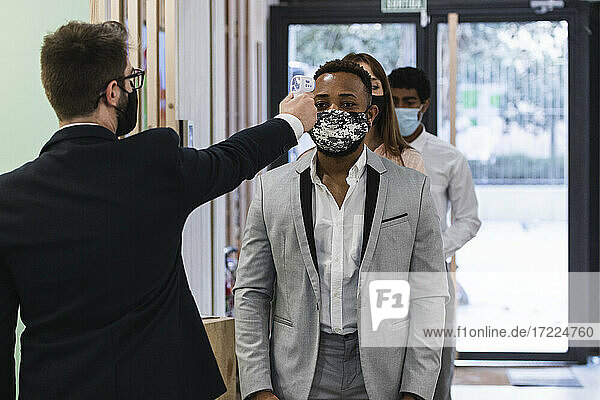 Mann mit Gesichtsmaske prüft die Temperatur eines Kollegen mit einem Infrarotthermometer im Büro
