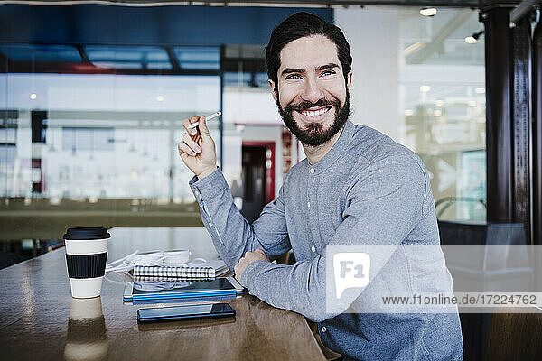 Lächelnder Freiberufler mit digitalisiertem Stift  der am Arbeitsplatz wegschaut