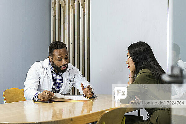 Male doctor explaining young female patient over medical record at clinic