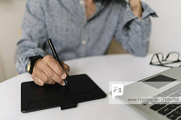 Männlicher Geschäftsmann  der ein Grafiktablett neben einem Laptop auf einem Tisch im Heimbüro benutzt