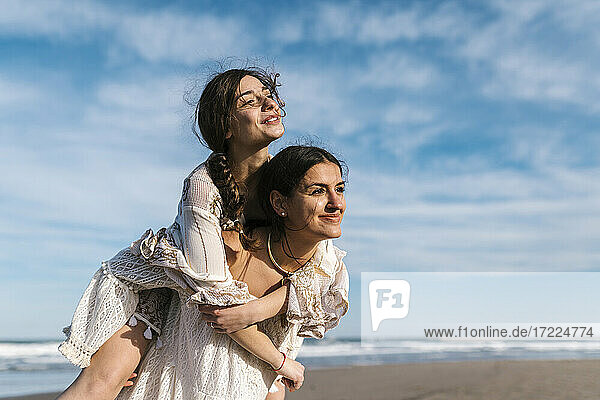 Young woman looking away while piggybacking female friend at beach