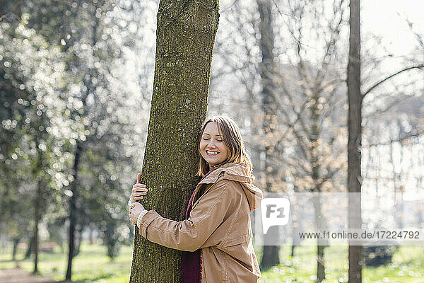 Glückliche erwachsene Frau  die einen Baum umarmt  während sie im Park steht