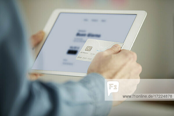 Männlicher Freiberufler  der mit einer Kreditkarte bezahlt  während er ein digitales Tablet im Büro benutzt