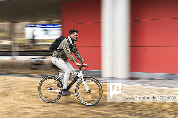Handsome man riding bicycle by red wall