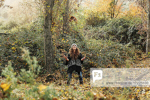 Verspielte Frau wirft Herbstblätter  während sie im Wald steht