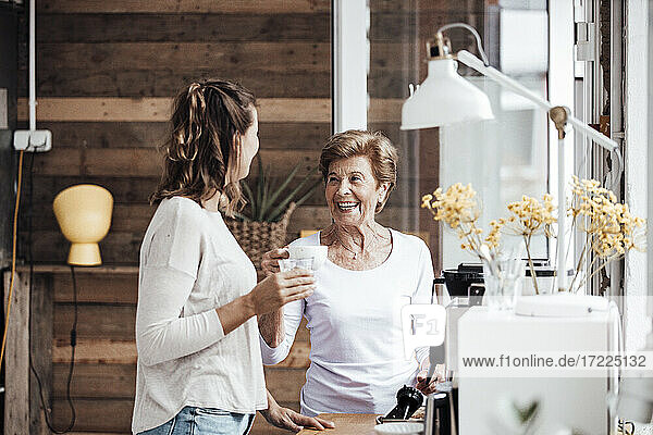 Cheerful woman with granddaughter having coffee at home