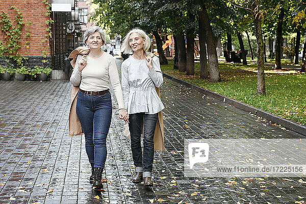 Lächelnde Freundinnen beim Spaziergang auf einem nassen Fußweg im Herbst