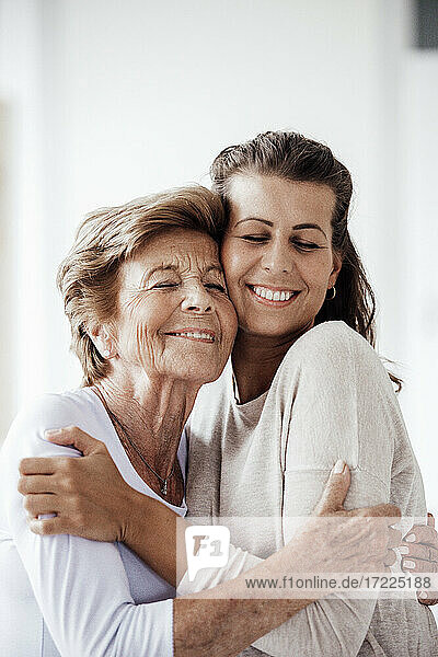 Smiling woman and granddaughter embracing each other at home