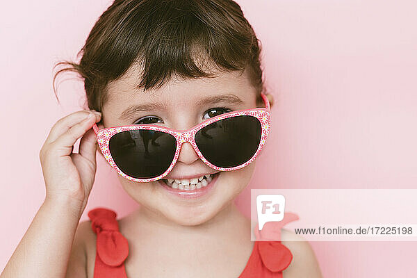 Porträt eines glücklichen kleinen Mädchens mit Sonnenbrille vor rosa Hintergrund