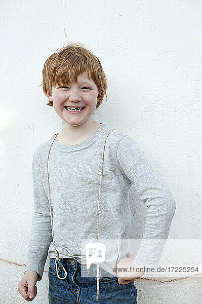 Lächelnder rothaariger Junge steht vor einer Wand im Freien