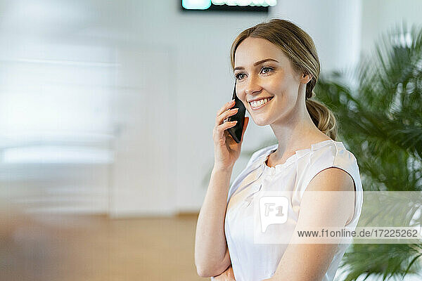 Lächelnde weibliche Fachkraft  die im Büro mit einem Mobiltelefon spricht