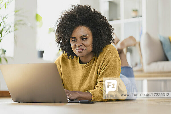 Smiling woman using laptop while lying down at home