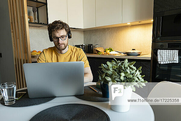 Geschäftsmann mit Kopfhörern  der zu Hause an seinem Laptop arbeitet