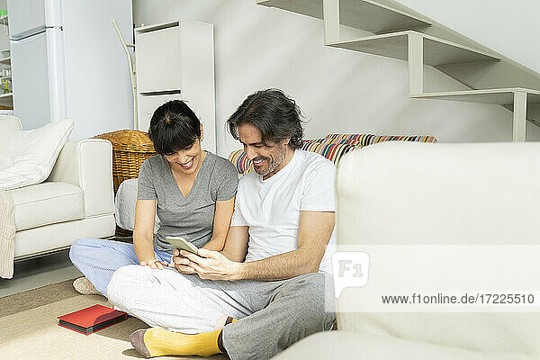 Fröhliches Paar benutzt sein Smartphone  während es zu Hause sitzt