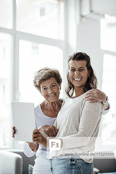 Fröhliche junge Frau hält digitales Tablet bei ihrer Großmutter zu Hause