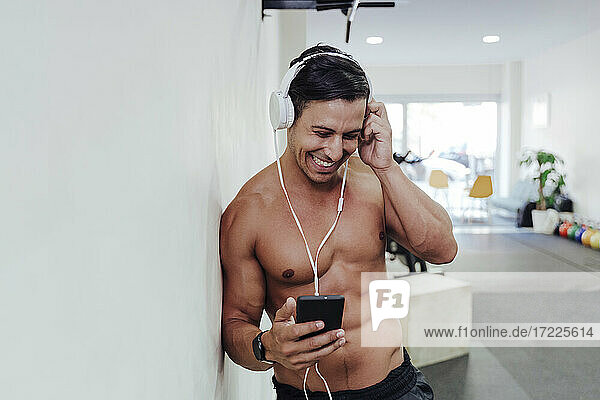 Male athlete adjusting headphone while using mobile phone in gym