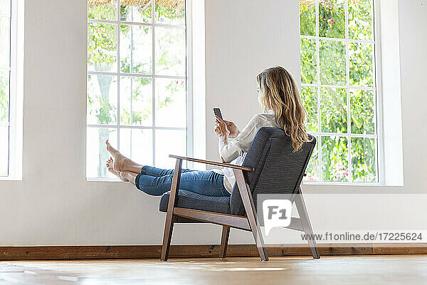 Frau  die ein Mobiltelefon benutzt  während sie sich auf einem Sessel zu Hause entspannt